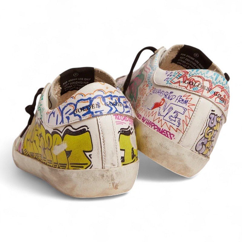 The Super-Star sneakers feature a white leather upper adorned with a vibrant multicolored graffiti print