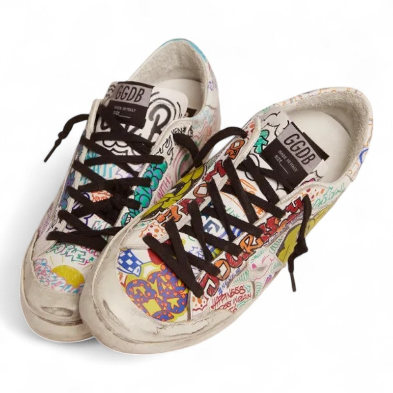 The Super-Star sneakers feature a white leather upper adorned with a vibrant multicolored graffiti print