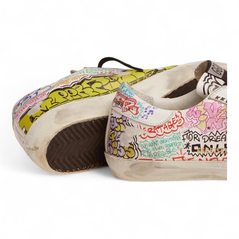 The Super-Star sneakers feature a white leather upper adorned with a vibrant multicolored graffiti print
